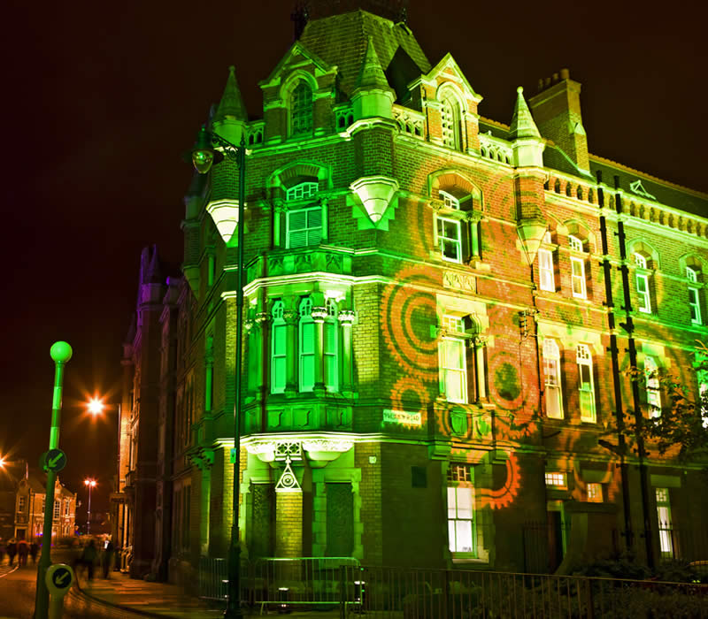 Historic building illuminated with green and orange lighting, showcasing architectural details, situated in an urban setting, reflecting Midas Productions' commitment to innovative solutions and event support.