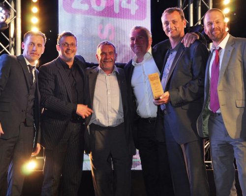 Group of men celebrating an award presentation at an event, with a backdrop displaying "2014" and bright stage lighting, emphasizing Midas Productions' recognition in the event industry.