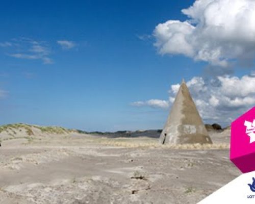 Deserted landscape featuring a conical structure on sandy terrain, with a clear blue sky and scattered clouds, relevant to Midas Productions' involvement in outdoor events and installations.