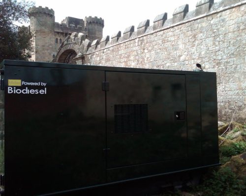 Generator powered by biodiesel in front of a historic stone wall and castle archway, relevant to Midas Generator Hire's services in power generation for events.