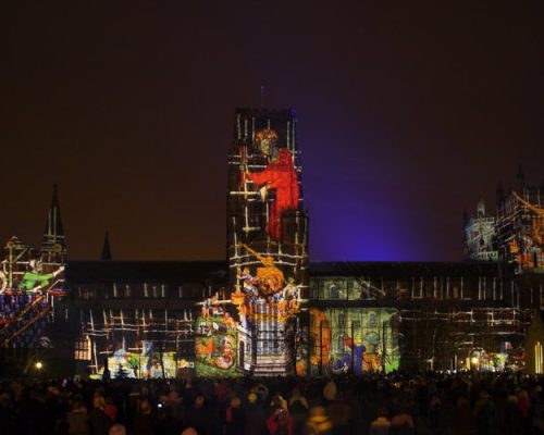 Durham Lumiere event featuring vibrant light projections on historic architecture, with crowds gathered to enjoy the spectacle, showcasing Midas's role as the power provider.