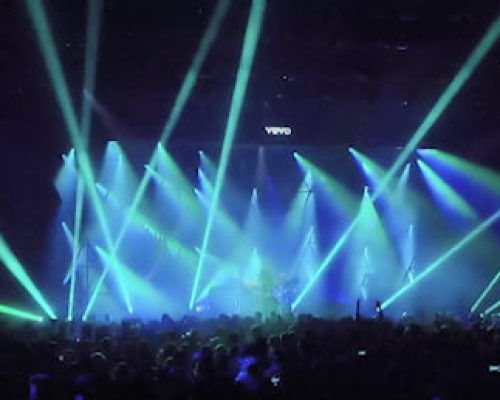 Concert scene with dynamic blue and green stage lighting, audience enjoying live performance, showcasing Midas's power solutions for events.