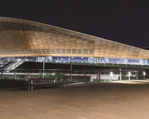 Modern architectural structure at night, featuring a sweeping roof design and illuminated pathways, relevant to Midas Generator Hire's outdoor power solutions for events.
