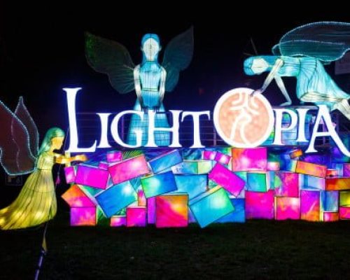 Lightopia festival display featuring illuminated figures and colorful lanterns, showcasing the event's branding and artistic installations.