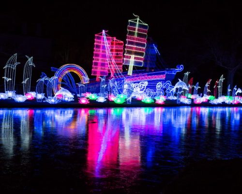 Colorful illuminated ship display with vibrant lights, reflecting on water, showcasing festive decorations for outdoor events, relevant to Midas's power solutions for lighting installations.