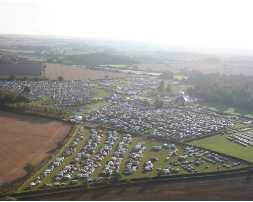 Aerial view of Shambala Festival site in Norfolk, featuring extensive parking areas filled with vehicles amidst a scenic landscape, showcasing Midas's role as the main power provider for the event.