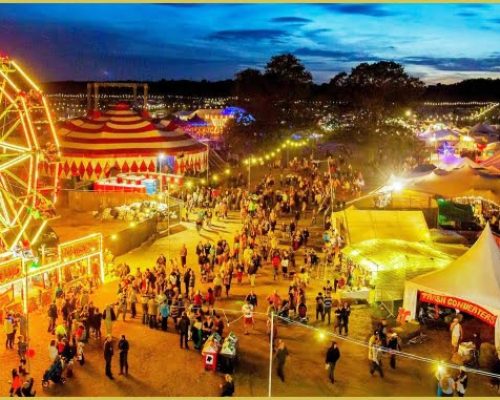 Festival scene at dusk featuring a vibrant Ferris wheel, illuminated tents, and crowds enjoying outdoor festivities, relevant to Midas Generator Hire's event power solutions.