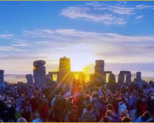Crowd gathered at Stonehenge during sunrise, with sunlight illuminating the ancient stones and a vibrant sky, showcasing Midas Generator Hire's involvement in heritage events.