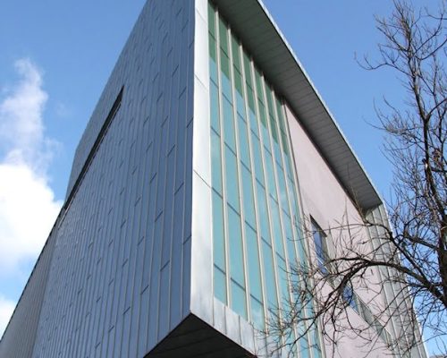 Modern architectural building with large glass windows, featuring a sleek metallic facade, surrounded by trees, representing venues for events and performances.