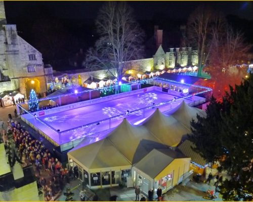 Winchester Cathedral Christmas Market featuring an illuminated ice skating rink surrounded by festive stalls and trees, capturing a vibrant winter atmosphere.